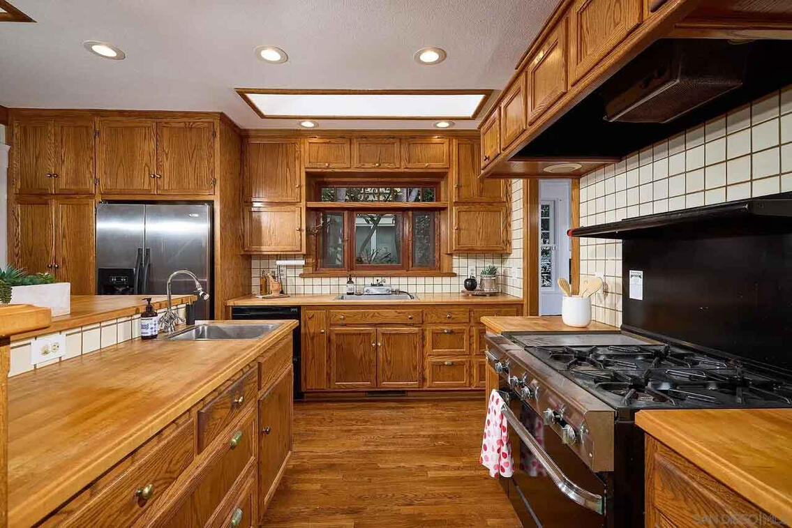 Spacious kitchen with floor-to-ceiling oak cabinetry, white tile backsplash, butcher block countertops, stainless steel appliances, gas range, and recessed lighting with skylight